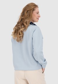 Felpa azzurra chiara con collo rotondo e maniche lunghe, dotata di tasca laterale e texture morbida, mostrata da un'angolazione laterale.