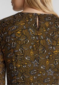 Brun mönstrad tyg med blommönster i gult och vitt. Har en knappstängning och nyckelhålsdetalj på baksidan.