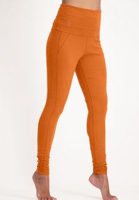 Orange leggings med hög midja, tillverkade av ett mjukt tyg, med sömdetaljer och en liten logotyp på midjeresåren.