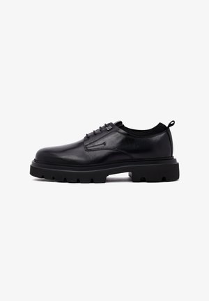 Schwarze Leder-Schnürschuhe mit dicker, robuster Sohle und Zuglasche an der Ferse, im Profil vor einem weißen Hintergrund dargestellt.