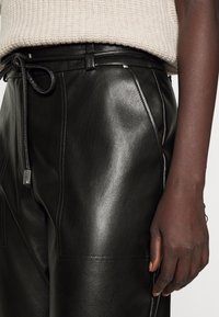 Svarta läderbyxor med en slät yta, med dragsko i midjan och synliga sömdetaljer längs sidorna.