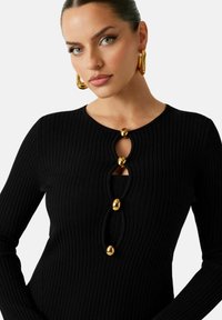 Sort ribbet langærmet top med huldesign og tre gyldne runde knapper foran samt rund halsudskæring.