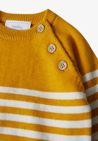 Maglione giallo a maglia con strisce orizzontali bianche, dotato di tre bottoni decorativi sulla spalla sinistra e un colletto a costine.