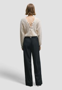 Pull beige clair en maille avec un dos décolleté et un détail lacé. Associé à un pantalon large noir à fines rayures. Texture lisse, coupe décontractée.