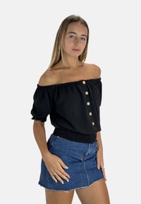 Schwarzes schulterfreies Oberteil mit elastischen Bündchen und Bund, vorne mit Holzknöpfen. Kombiniert mit einem hellblauen Jeansrock.