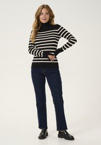 Crna i krem prugasta rolka sa dugim rukavima, uparena s tamnoplavim ravnim trapericama i crnim cipelama. Glatka tekstura.