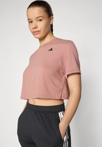 Camiseta rosa recortada hecha de tela suave, con un escote redondo y mangas cortas, con un acento de logo negro en el pecho. Pantalones de chándal negros con rayas blancas.