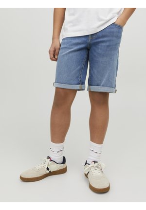 Lyseblå denimshorts med opbrettede manchetter, kombineret med hvide sokker med et maritimt mønster og beige sneakers med mørke detaljer.
