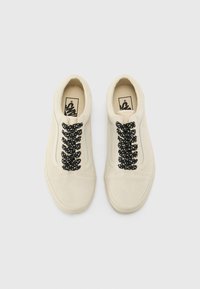 Beige suede sneakers with black textured laces, rounded toe, and low profile design. Features classic branding on the insole.