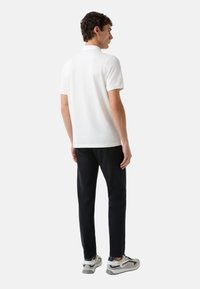 Witte polo met korte mouwen, gecombineerd met donkere broeken en sportschoenen met grijze, marineblauwe en witte accenten.