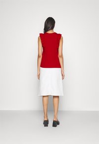 Červený bezramínkový top s volánkovými detaily na ramenou, doplněný bílou sukní po kolena a černými botami na blokovém podpatku.