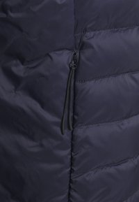 Dunkelblaue Steppjacke mit horizontalem Steppmuster, glattem Nylonfinish und einem seitlichen Reißverschluss mit Ziehlasche.