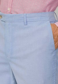 Jasnoniebieskie spodnie w paski z płaskim przodem, kieszeniami bocznymi i elastycznym paskiem w talii. Materiał ma gładką fakturę z delikatnymi pionowymi paskami.