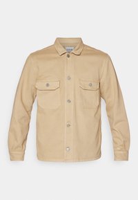 Beige denimjacka med knäppning framtill, två bröstfickor och krage. Har långa ärmar och silverfärgade detaljer.