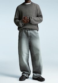 Pull gris côtelé avec une coupe ample et un col rond, associé à un jean délavé gris clair oversize. Des baskets noires complètent la tenue.