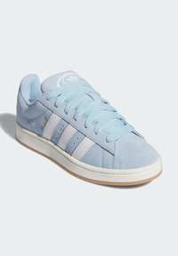 Light blue suede sneaker with three white stripes, lace-up design, padded collar, and beige rubber outsole. Features logo on tongue.