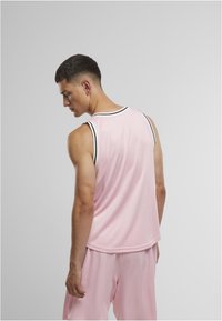 Débardeur de sport sans manches rose avec un col rond, présentant des rayures noires et une coupe ample, fabriqué en tissu respirant.
