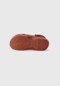 Brown rubber footwear sole with textured tread pattern, curved shape, and a strap. Features "crocs" branding near the heel.