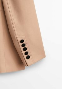 Manica di una giacca beige con cinque bottoni neri disposti in una fila verticale vicino al polsino, su uno sfondo bianco.