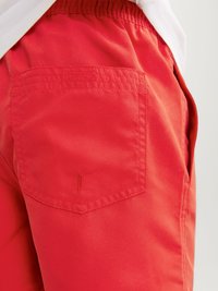 Pantaloni corti rossi realizzati in tessuto leggero, con una cintura elastica e una tasca posteriore con un semplice dettaglio di cucitura.