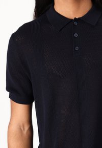 Námornícky pletený polo s textúrovaným vzorom, krátkymi rukávmi, gombíkovou lištou a rebrovanými doplnkami po stranách.