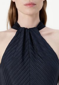 Navy halter top with wavy pleats, featuring a knotted neckline design. The fabric has a subtle sheen and textured finish.