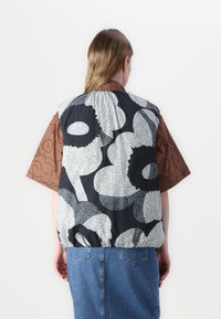 Vadderad väst med ett djärvt svartvitt blommönster, parat med en brun kortärmad skjorta med en kontrasterande design.