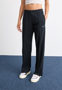 Black sweatpants in a relaxed fit, made of soft fabric with an elastic waistband. Features a small white Nike logo on the left side.