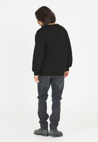 Musta collegepusero, jossa on roikkuvat hartiat, ribbattu hihansuu ja helma. Yhdistetty slim-fit tummanharmaisiin farkkuihin ja mustiin nilkkabootseihin.