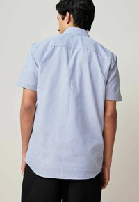 Chemise à manches courtes avec des rayures verticales bleues et blanches, un col boutonné et un ourlet arrondi. Fabriquée en tissu léger.