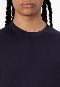 Pull en maille bleu marine avec un col rond côtelé et une texture lisse. Gros plan montrant l'absence de motifs et un minimum de détails.