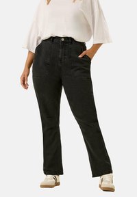 Svarta högmidjade jeans med stora framfickor, en figurnära silhuett och mjuk textur. Kombinerat med en lös vit topp och sneakers.