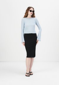 Light blue ribbed long-sleeve top with flared cuffs, paired with a black ribbed knee-length skirt. Black flip-flops and sunglasses complete the look.