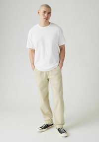 Vit bomullströja i kombination med ljusbeige chinos och svarta sneakers. Enkelt design, avslappnad passform, klassisk färgkombination.