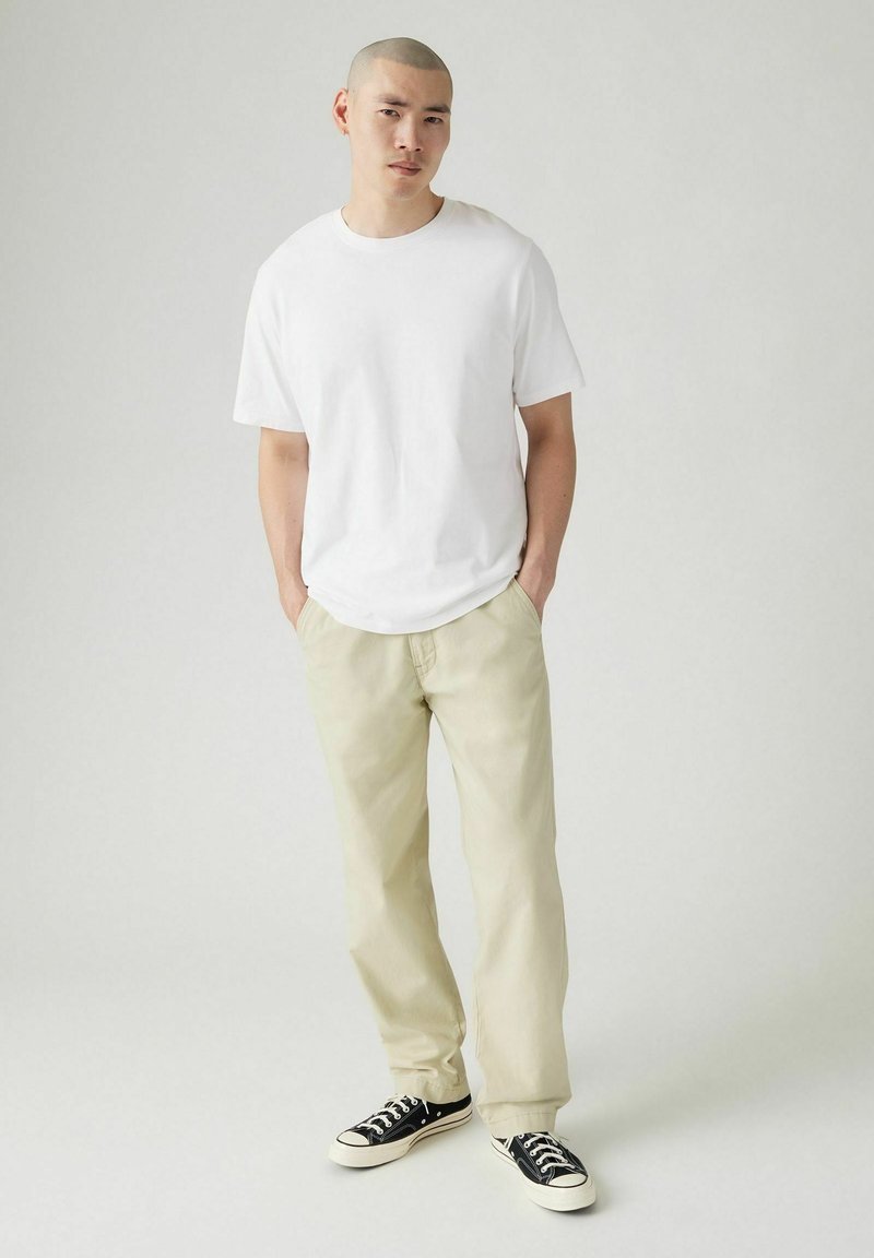 Camiseta de algodón blanca combinada con chinos beige claros y zapatillas negras. Diseño simple, corte relajado, combinación de colores clásica.