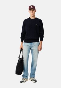 Marineblå kabelstrikket genser, lyseblå jeans, svart duffelbag og grå joggesko. Burgunder lue med hvit "L." En enkel og uformell antrekk.