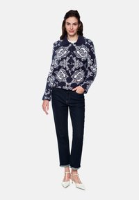 Navy sweater with white floral pattern, collared design, long sleeves. Paired with dark jeans and white pointed-toe heels.