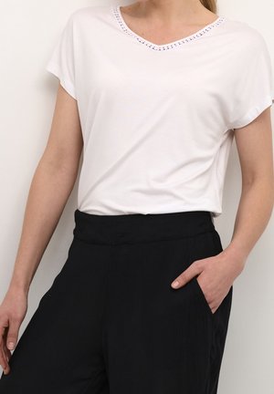 Biała koszulka z krótkim rękawem i dekoltem w kształcie V, ozdobiona dekoracyjnym wykończeniem. W parze z czarnymi, luźnymi spodniami z boczną kieszenią.