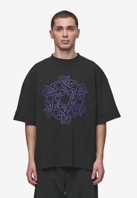 Black oversized t-shirt made of cotton, featuring a central purple graphic design with intertwining shapes and patterns. Short sleeves, crew neck.