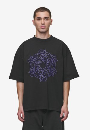 T-shirt noir oversize en coton, featuring un design graphique central violet avec des formes et motifs entrelacés. Manches courtes, col rond.
