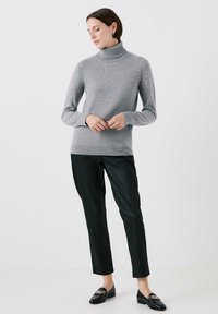Grå turtlenecktröja i stickad material, med långa ärmar och en figurnära design, tillsammans med svarta skräddarsydda byxor och loafers.