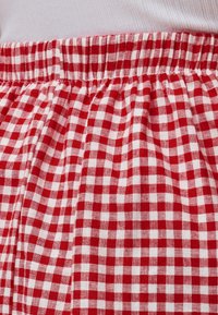 Ceinture d'un vêtement en tissu à carreaux rouges et blancs avec un détail élastique froncé et un tissu côtelé blanc au-dessus.