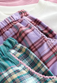 Drie gevouwen geruite pyjamabroeken in paarse, groene en roze tinten met elastische taillebanden, samen met witte en roze sweaters.