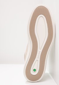 Light tan sneaker sole with wavy tread pattern, featuring a white midsole and a green hexagonal accent. Text reads "Timberland."