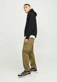 Zwarte hoodie met een voorzak, gedragen over een wit T-shirt, gecombineerd met olijfgroene cargobroeken met meerdere zakken. Zwarte en grijze sneakers.