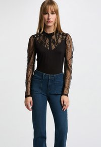 Body nero con maniche trasparenti a pois e scollatura in pizzo. Abbinato a jeans blu a vita alta. Tessuto di trama liscia.