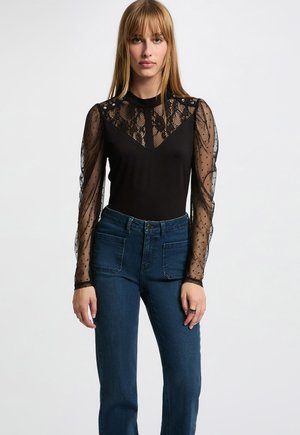 Body noir avec des manches transparentes à pois et un empiècement en dentelle. Associé à un jean bleu taille haute. Texture de tissu lisse.