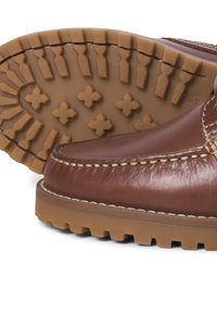 Chaussure en cuir marron avec semelle en caoutchouc épaisse et rainurée, présentant des motifs de crampons croisés et rectangulaires pour une meilleure adhérence et durabilité.