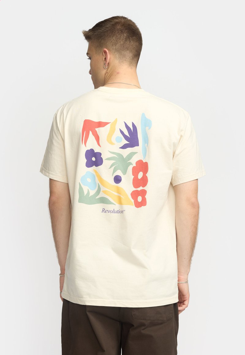 Beige bomuld t-shirt med et flerfarvet abstrakt blomst- og bladdesign på ryggen. Inkluderer teksten "Revolution" i lilla.