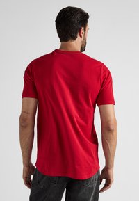 Rode katoenen T-shirt met korte mouwen, ronde hals en een iets langere achterkant. Soepele textuur zonder zichtbare patronen of accenten.